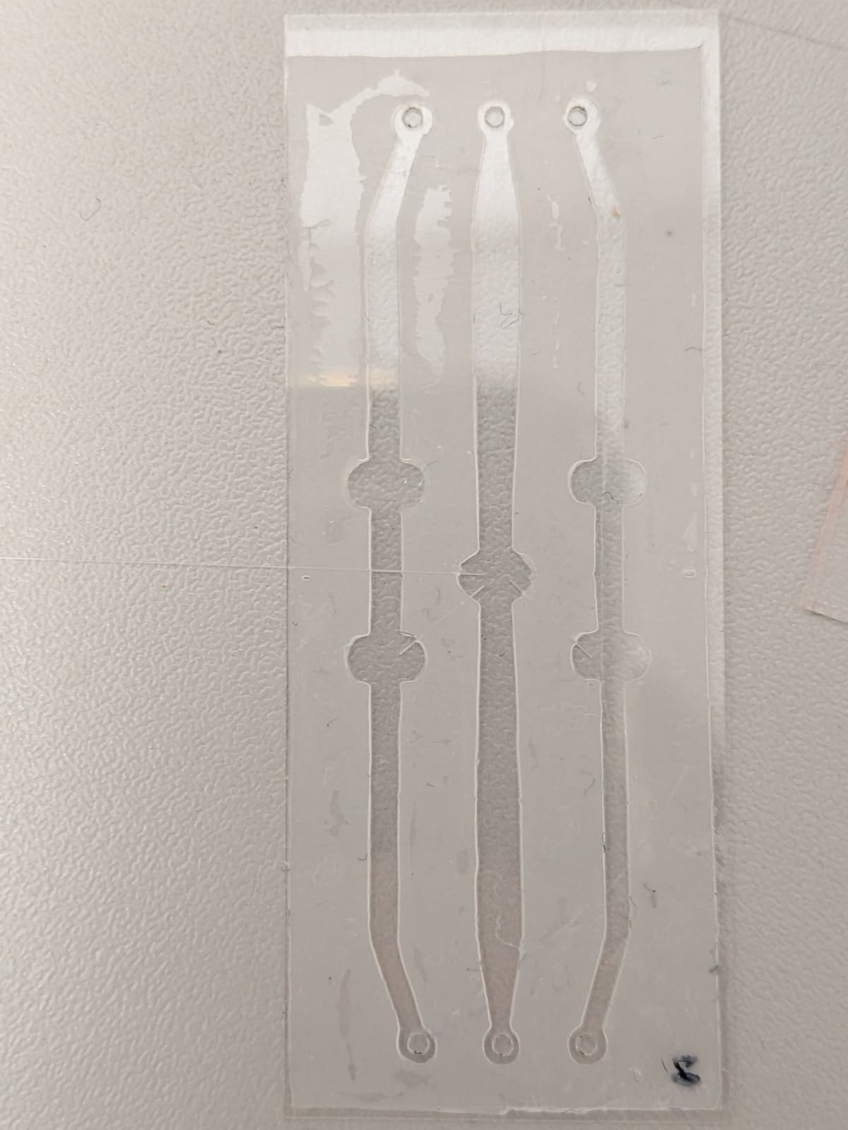 A glass microfluidic chamber with three channels, standing against a white wall