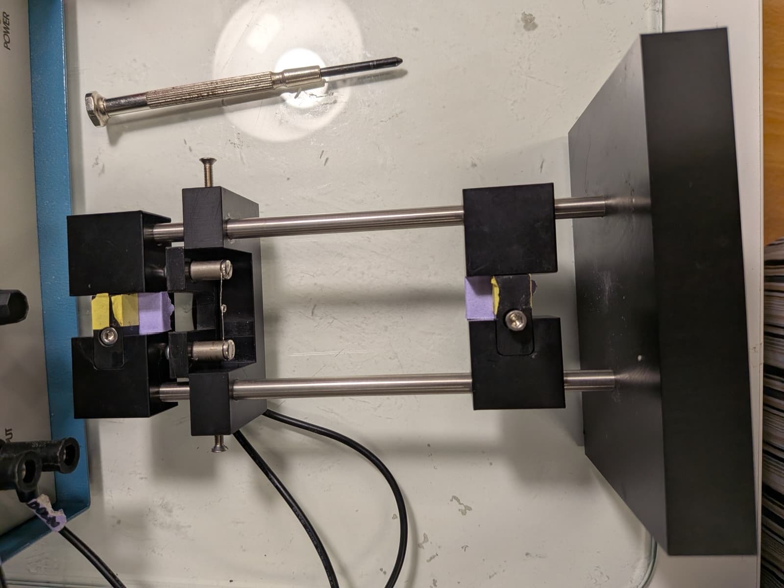 A handmade pipette puller: two clamps on steel rods, with purple tape holding a glass micropipette